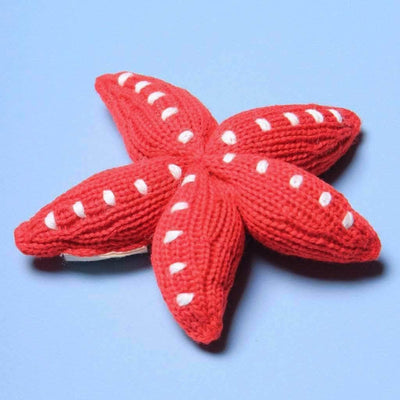 Knitted red starfish rattle with white accent dots. Shown on a light blue background.