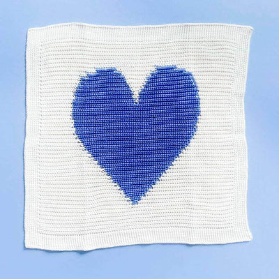  Cream, ribbed baby blanket with large blue heart in the center. Shown on a bright blue background.