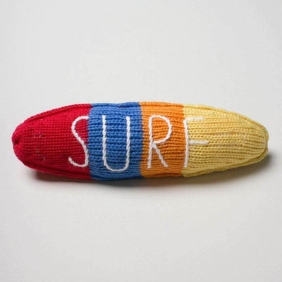 Knitted surf board rattle in colorblocks of red, blue, orange and yellow with the word "surf" top stitched on it. Shown on a neutral background.