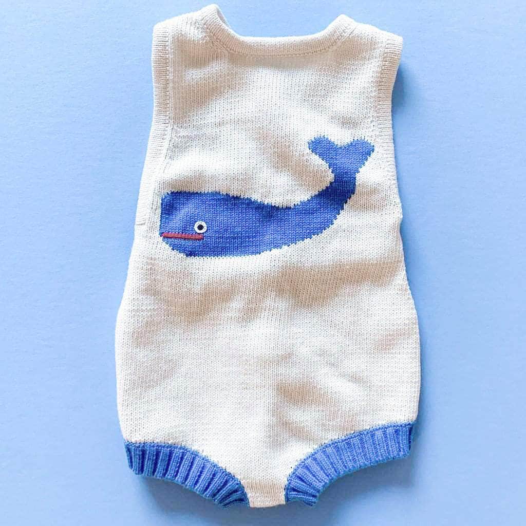 Cream knitted summer romper with large, French blue whale in the center. Leg holes are ribbed with the same blue color. Photographed on a bright blue background.