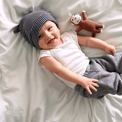 Monkey baby gifts. Newborn rattle toy in organic cotton laying next to a smiling child.